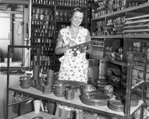 Woman marking pottery in a storage room containing numerous completed pottery items, c. 1930