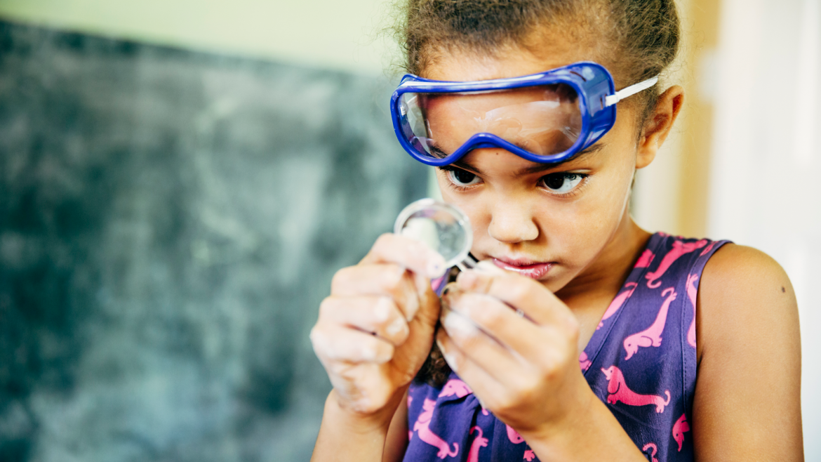 Young girl with goggles looking through magnifying glass