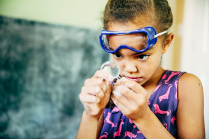 Young girl with goggles looking through magnifying glass