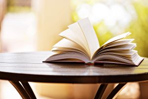 A hardback book lies open on a table against a soft-focus garden background