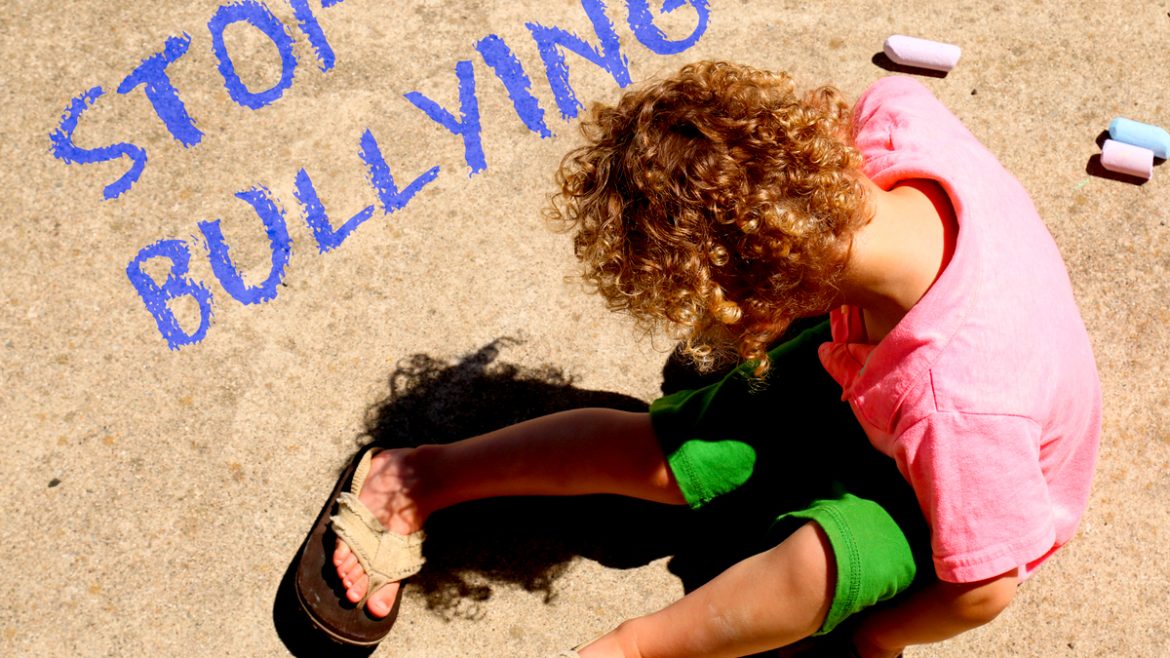 Sad child on ground with Stop Bullying written in chalk