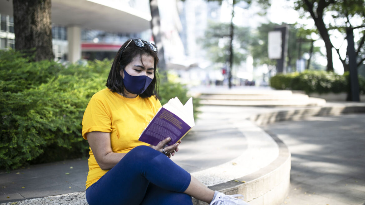 Asian female reading a book on the sidewalk