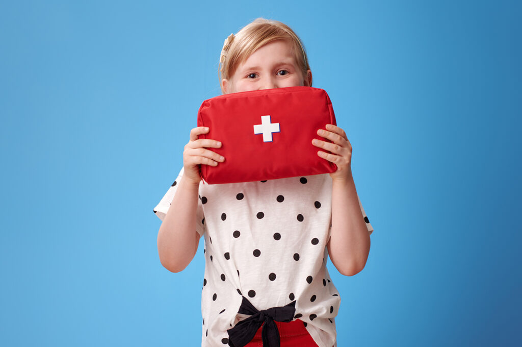 happy child holding first-aid kit in front of face on blue