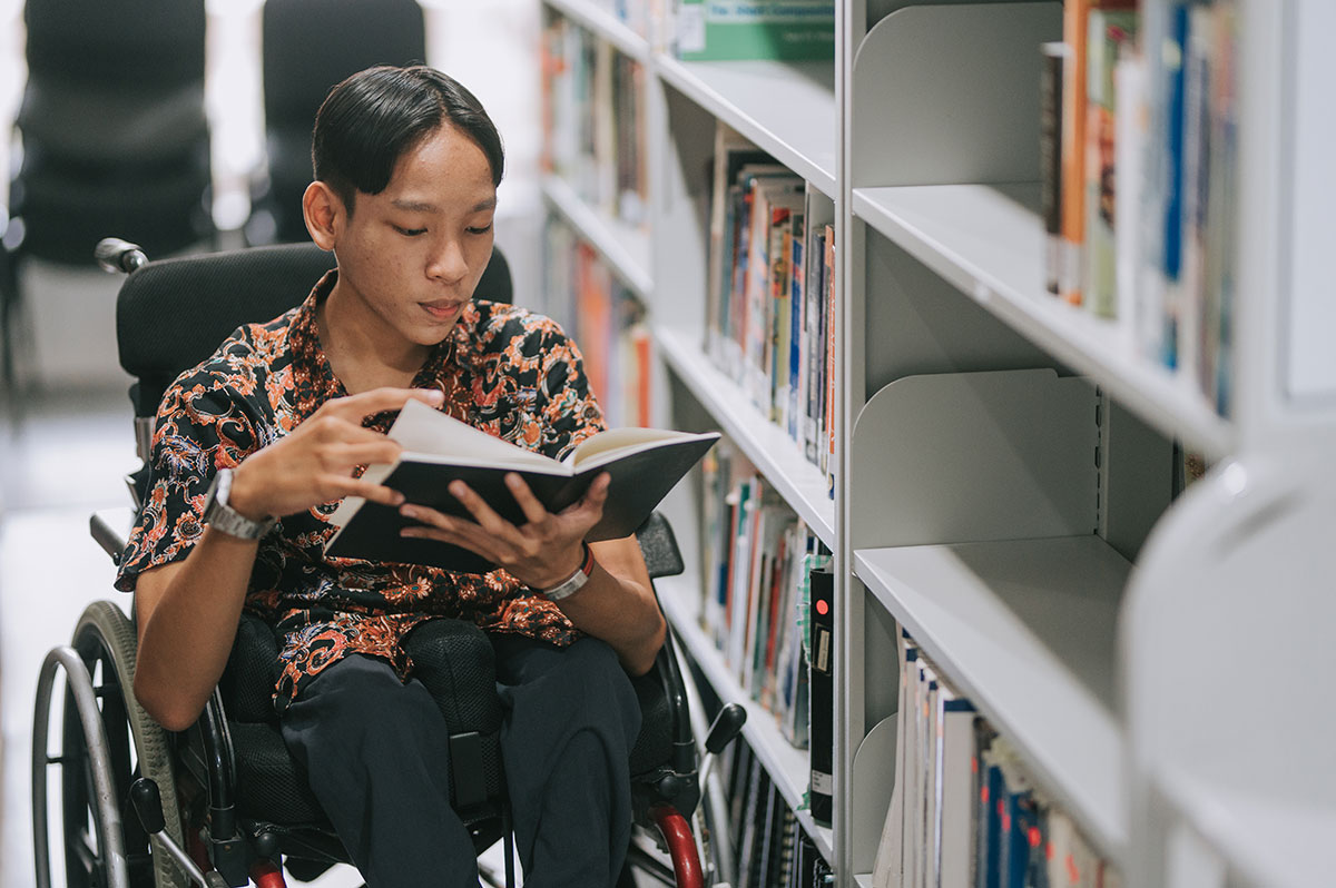 young man in wheelchair reading at the library