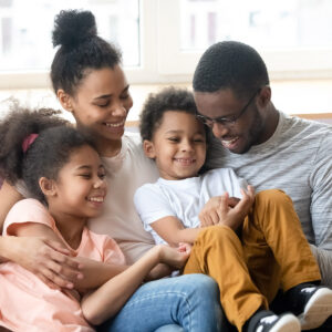 African ethnicity parents pre-teen daughter little son having fun sitting on couch tickling each other laughing enjoy priceless time together. Affection and connection, family ties and bond concept
