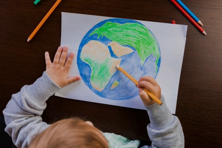 child drawing the earth with colored pencils