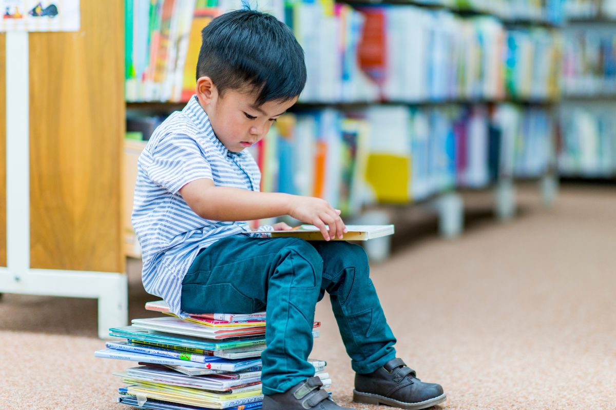 child sitting on stack of books at library